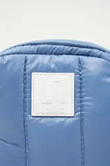 Bandolera azul con diseño capitoneado, correa de soga en blanco y negro, y logo rectangular blanco en la parte frontal.