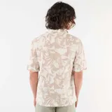 Camisa de manga corta color beige con estampado abstracto de hojas blancas, cuello camisero abierto y cierre frontal de botones.