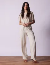 Pantalón cargo de lino a rayas verticales grises y blancas, marca Marissa Olivia. Pretina ancha elastizada con lazo de ajuste, bolsillos inclinados delanteros y bolsillos laterales con botón.