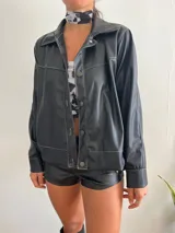 Campera negra de cuero sintético con costuras blancas a contraste, cierre con botones metálicos y cuello clásico.