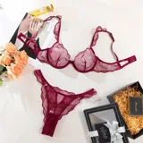 Conjunto de lencería de tul translúcido color bordó con diseño de líneas orgánicas, compuesto por soutiene con aros y breteles con volados, y bombacha colaless ajustable con detalles de argollas doradas.