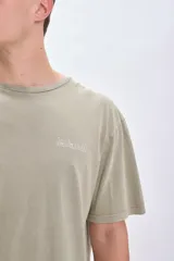 Camiseta manga corta oversize color verde con estampado de una pieza de rompecabezas con una flor en su interior y la palabra 'Island' debajo.