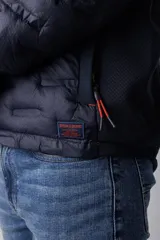 Campera de nylon termosellada con capucha, color azul marino, con cierre frontal y detalles en color naranja en el borde del cierre y costuras de la capucha.