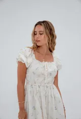 Vestido corto color crema con estampado floral, escote cuadrado con lazo ajustable, mangas cortas abullonadas y corte princesa.