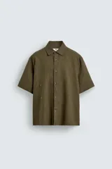 Camisa de corte relajado confeccionada en lino color verde militar, con cuello solapa, manga corta y cierre frontal de botones.