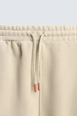 Bermuda de algodón color beige, estilo jogger, con corte relajado, cintura elástica ajustable con cordón y bolsillos laterales y trasero.