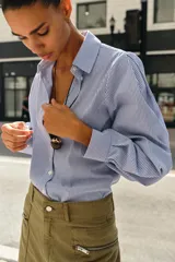 Camisa de manga larga con cuello solapa, cierre frontal con botones y bajo asimétrico, con estampado de rayas verticales.