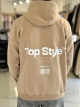 Canguro oversize de color tostado con capucha, diseño amplio y estampado gráfico en la espalda con texto y código de barras.