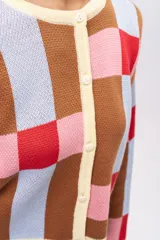 Saco tipo cardigan de tejido de punto con diseño geométrico de cuadros en tonos marrón, celeste, rosa y rojo. Presenta cuello redondo, cierre frontal con botones y terminaciones en color crema.