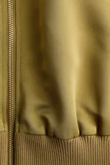 Campera bomber de tejido grueso color verde militar, con cuello corto acanalado, cierre frontal y bolsillos insertados. Cuenta con hombros caídos, mangas abullonadas y puños y bajo acanalados.