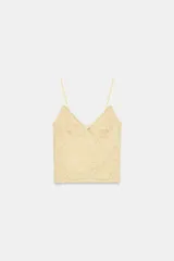 Top de encaje con escote en pico y tirantes finos ajustables. Presenta un pequeño lazo decorativo en el centro del escote y un diseño de encaje floral en toda la prenda.