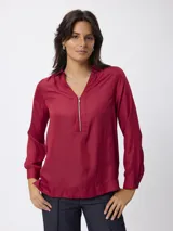 Blusa de manga larga color bordó, con cuello camisero y cierre frontal parcial con cremallera metálica. Presenta puños abotonados y un corte recto.