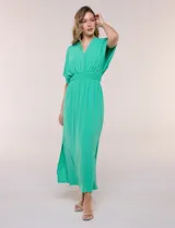 Vestido largo amarillo de corte fluido con escote en V, mangas cortas amplias y apliques de tachas en el escote y puños. Posee cintura elastizada fruncida y falda larga con tajos laterales en el ruedo.