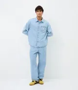 Camisa masculina de corte boxy confeccionada en denim de algodón, con cuello camisero, mangas largas, cierre frontal con botones y bolsillo funcional en el pecho.