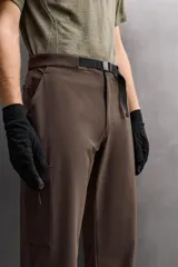 Pantalón de hombre color marrón oscuro, corte regular fit, confeccionado en tejido técnico compacto elástico. Presenta cintura ajustable con cinturón negro a contraste, bolsillos frontales, bolsillo trasero con cierre y bolsillo cargo con cierre en la pernera.