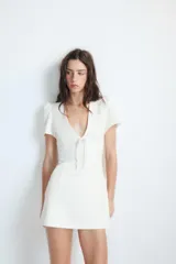 Vestido corto de Zara, color blanco, con escote en pico, mangas cortas abullonadas y detalle de lazo frontal en el mismo tejido. Presenta un corte entallado y cierre de cremallera oculta en la espalda.