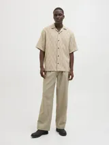 Camisa de manga corta Jack & Jones con cuello resort y cierre de botones. Diseño con estampado de espiga en tonos beige y blanco. Confeccionada en tejido dobby 100% algodón.