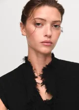 Top de tweed negro con cuello en V, diseño cruzado y terminaciones deshilachadas. Presenta un corte entallado sin mangas y detalle fruncido en la parte frontal.