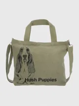 Cartera tipo tote bag de lona color verde oliva, con estampado frontal de un perro Basset Hound y el logo de la marca. Cuenta con doble asa superior, correa ajustable y extraíble, cierre principal y bolsillos internos y externos.