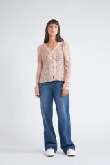Blusa rosa con estampado de flores blancas y amarillas, cuello en V, manga larga abullonada y cierre frontal con botones.