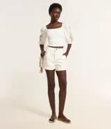 Short de sarga color blanco, con pliegues frontales, trabillas en la cintura, cierre tradicional, bolsillos y bordados delicados con temática de playa.