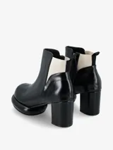 Bota corta tipo botineta de cuero negro con taco cuadrado y plataforma redondeada. Presenta un panel elástico lateral en color crema y tirador en la parte trasera.