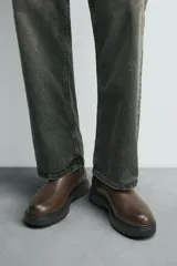 Bota tipo Chelsea de cuero color marrón oscuro, con paneles elásticos laterales, tirador trasero y suela track con volumen.