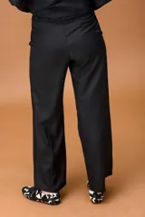 Pantalón sastrero de corte ancho y tiro alto, con diseño de líneas limpias, bolsillos laterales y cierre frontal con botón. Presenta una caída fluida y estructura amplia.