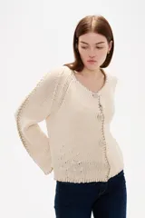 Cardigan de punto color natural, con cuello en V, cierre frontal con botones y diseño holgado. Presenta detalles de costuras decorativas bordadas a lo largo de las mangas y en los bordes.