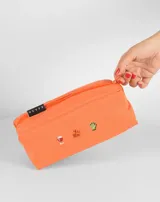 Neceser rectangular de tela color ladrillo con cierre superior y tres bordados pequeños: una hoja de arce, una taza de té y un croissant.