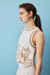 Blusa sin mangas de corte crop en color blanco, con detalles de bordados calados en tono tostado formando diseños florales en el cuello, los hombros y el borde inferior.