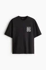 Remera de algodón en punto pesado color negro, de corte holgado con hombros caídos, cuello redondo acanalado y estampa frontal estilo universitario con el texto 'SOHO NYC 86'.