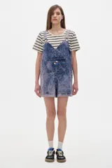 Mono enterito corto de denim azul con lavado ácido, corte oversized, tirantes regulables, bolsillo plaqué en el pecho y ruedo desflecado.