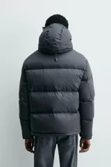 Cazadora acolchada tipo puffer de corte regular, confeccionada en tejido técnico repelente al agua. Cuenta con cuello subido, capucha ajustable y desmontable, cierre frontal con cremallera, bolsillos laterales con cremallera oculta y puños ajustables con tira adherente.