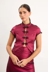 Top de tafeta elastizada color bordó, con cuello mao, mangas cortas, cierre frontal con botones de nudo chino y detalles de puntilla negra en los bordes.