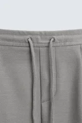 Bermuda negra de corte recto, con cintura elástica ajustable mediante cordón, pliegues frontales y bolsillos de vivo en la espalda. El bajo tiene un dobladillo vuelto.