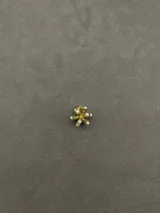 Dije con forma de flor dorada con pequeñas perlas blancas en los extremos de cada pétalo.