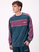 Buzo de cuello redondo marca Rusty, con diseño de bloques de color en azul petróleo y bordó, con detalles de líneas blancas y logo bordado en el pecho.