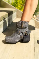 Botas cortas de cuero color marrón oscuro con hebillas y estribo desmontable.