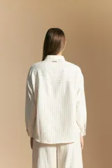 Camisa de manga larga color blanco hueso con finas rayas verticales en color oscuro. Presenta cuello camisero, botones frontales y dos bolsillos superpuestos en el pecho.