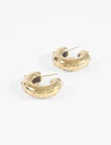 Par de aros tipo argolla gruesa de acero quirúrgico, color dorado, con pequeños puntos en relieve a lo largo de su superficie curva.