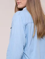 Campera de denim liviano azul, de corte clásico y silueta recta, con cuello camisero, cierre frontal con botones rústicos y bolsillos con solapa en el pecho.