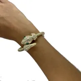 Pulsera rígida plateada con forma de serpiente, con cabeza y cola decoradas con strass y ojos de esmeralda.