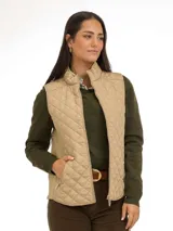 Chaleco sin mangas capitoneado en color beige, con cierre frontal y bolsillos laterales. Presenta un diseño entallado con cuello alto.