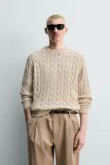 Sweater de punto con diseño de trenzas, color beige, cuello redondo y manga larga con terminaciones en rib.
