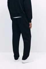 Pantalón jogger negro de corte regular fit, confeccionado en tejido suave con mezcla de algodón. Presenta pliegues cosidos en la parte delantera, cintura elástica con cordón ajustable, bolsillos laterales y un bolsillo insertado en la parte trasera.