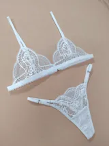 Conjunto de lencería de encaje blanco, compuesto por un corpiño triangular de tirantes regulables y una bombacha tipo colaless con tiras laterales ajustables.