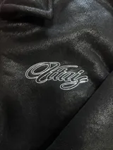 Campera de cuero sintético negro con diseño tipo bomber, cuello camisero y puños y ruedo elásticos. Presenta un bordado grande en la espalda con tipografía cursiva en color blanco.