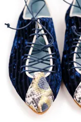 Zapato tipo blucher de terciopelo de seda azul marino con diseño rayado. Presenta una abertura central ajustable con cordones, ribetes en contraste y detalles en piel con estampado de pitón multicolor en la puntera y el talón. Cuenta con suela de cuero.
