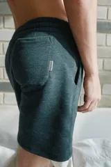 Bermuda de algodón y poliéster en color gris melange, con cintura elástica y bolsillos laterales. Presenta una etiqueta pequeña con el logo de la marca en el bolsillo trasero.